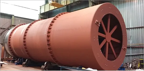 Velký průmyslový válcový kovový zařízení s červenohnědou barvou uvnitř výrobní haly.