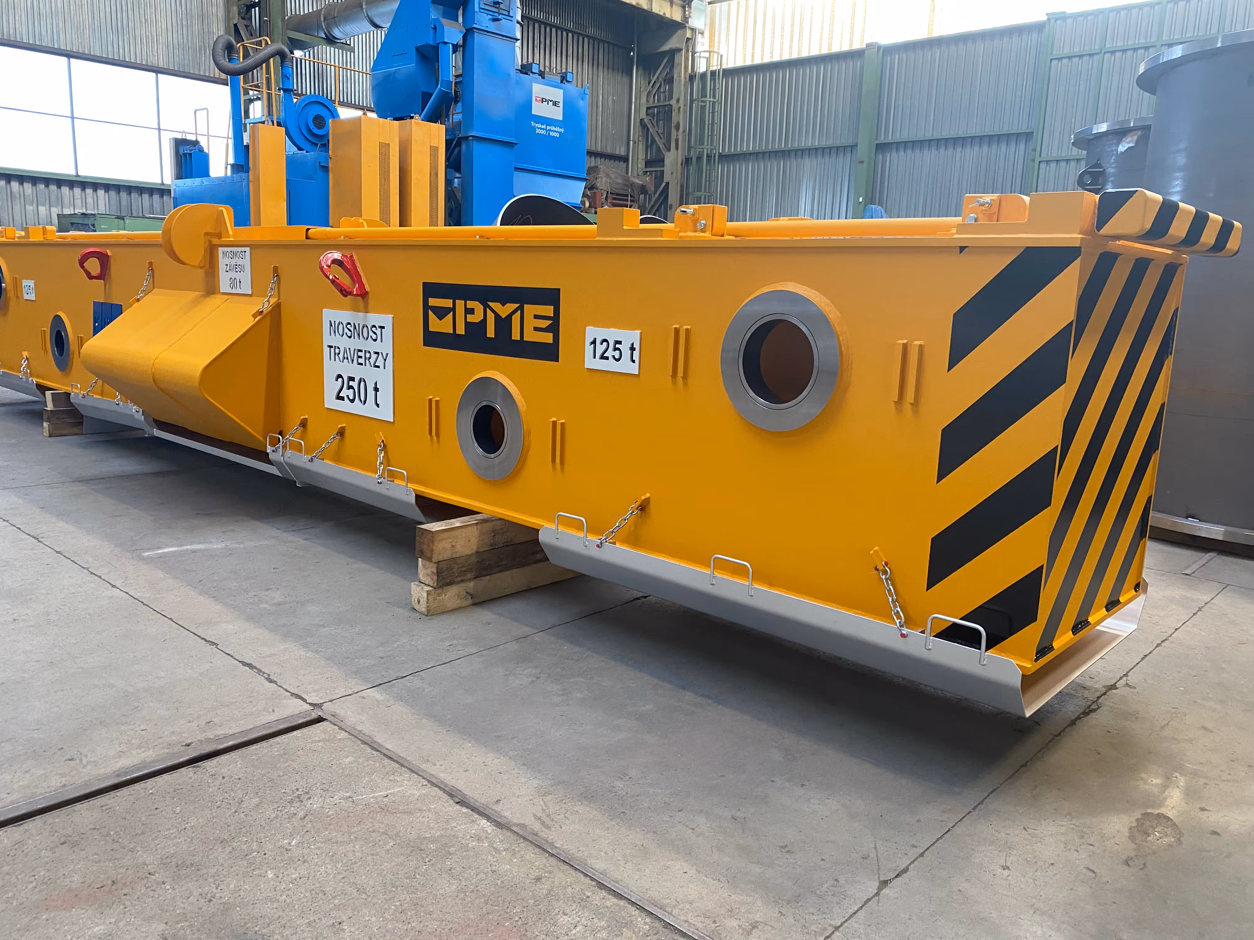 Žlutá průmyslová traverza s označením nosnosti 250 tun umístěná v dílně.