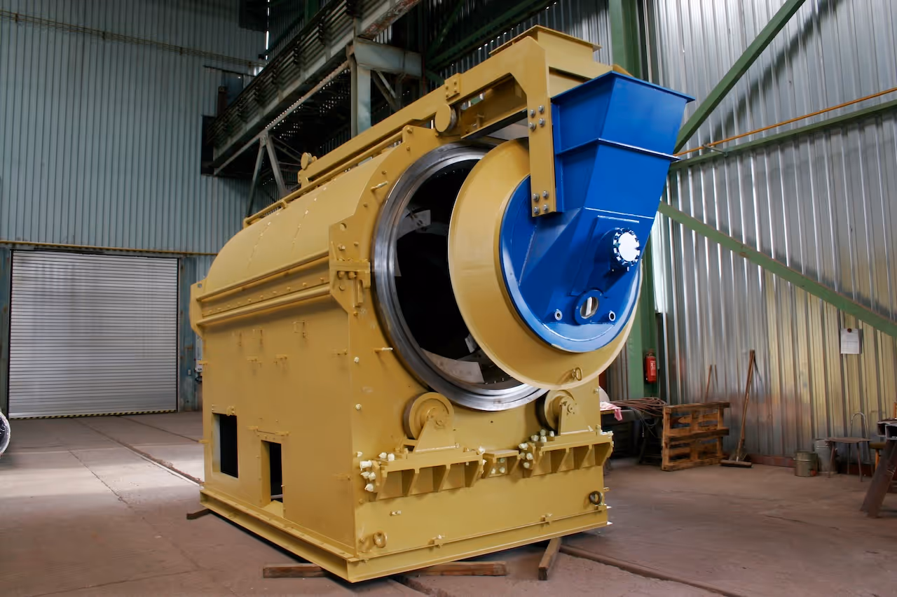 Velký průmyslový stroj žluté barvy s modrou nádržkou uvnitř kovové haly.