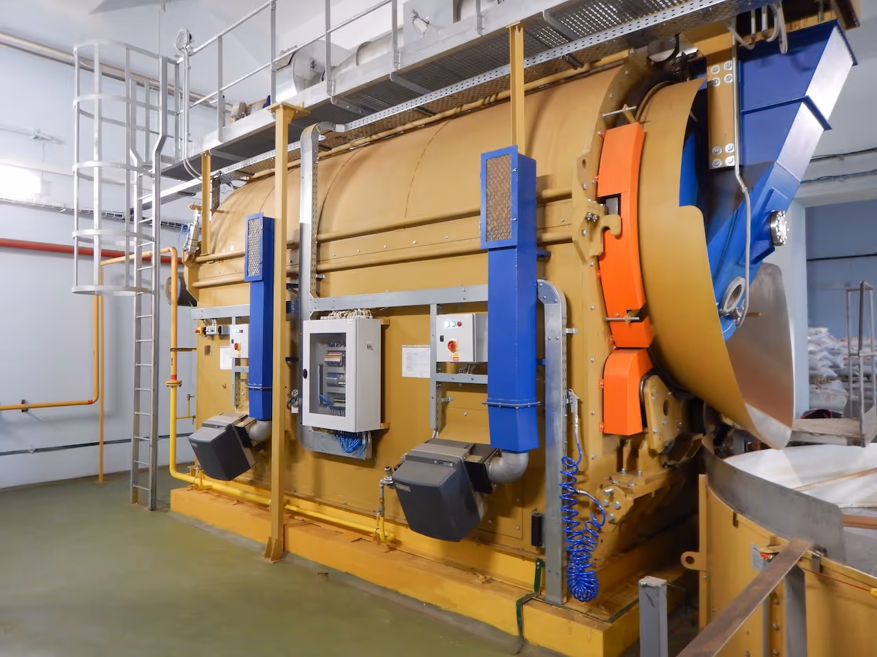 Průmyslový žlutý rotační sušička s modrými a oranžovými součástmi v čisté výrobní hale.