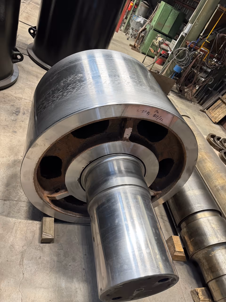 Lesklý kovový hřídel s velkým ložiskem uložený na podlaze průmyslové dílny.