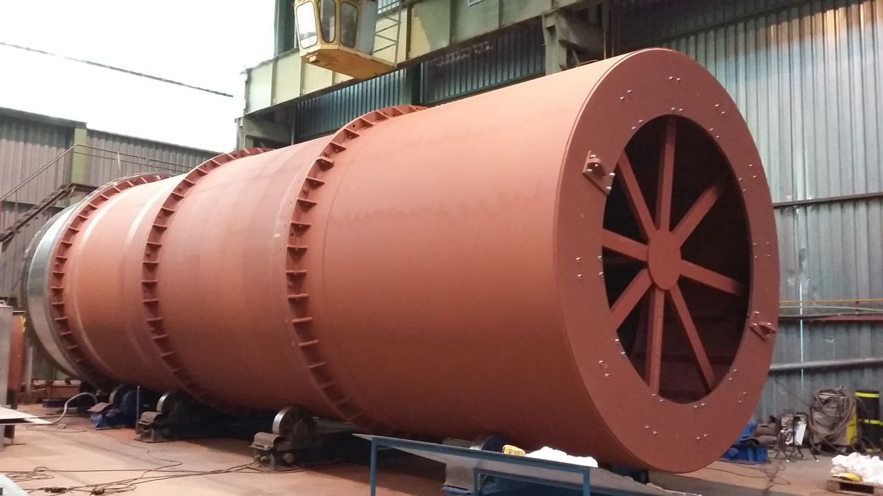 Velký průmyslový válcový kovový zařízení s červenohnědou barvou uvnitř výrobní haly.