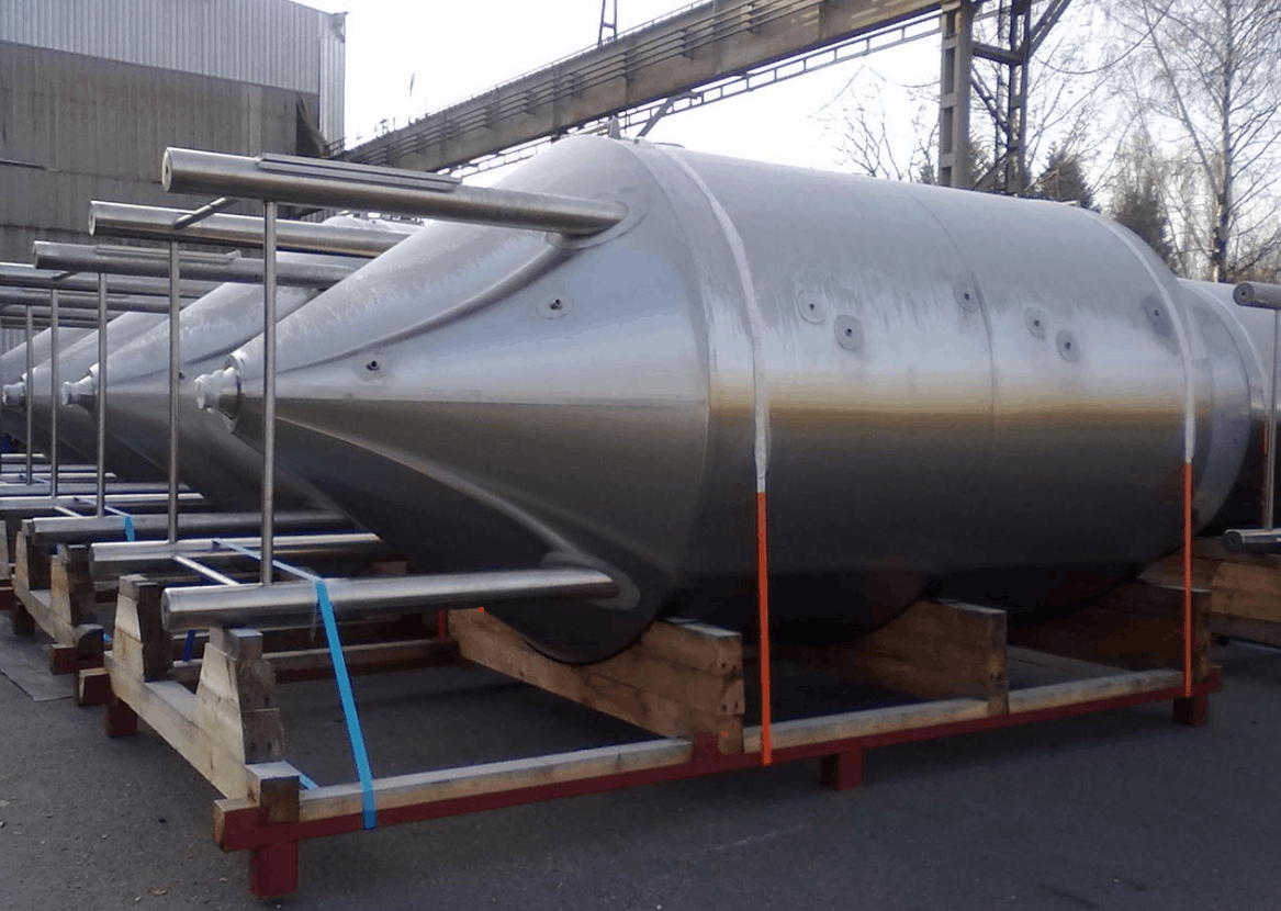 Dvě velké kovové průmyslové nádoby naložené na plošinovém návěsu na otevřeném prostranství.