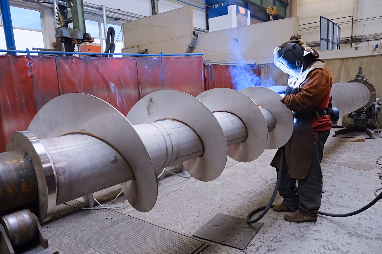 Large industrial cylindrical metal equipment with red-brown color inside the production hall.