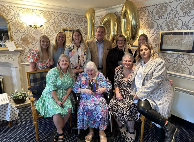 Group photo of a client celebrating her 100th birthday with friend's family indoors.
