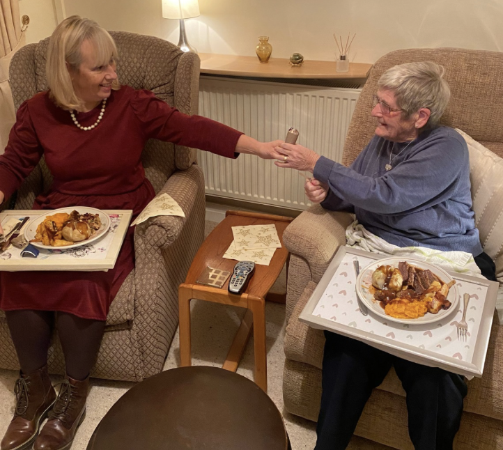 Two elderly clients sitting in armchairs sharing a meal.