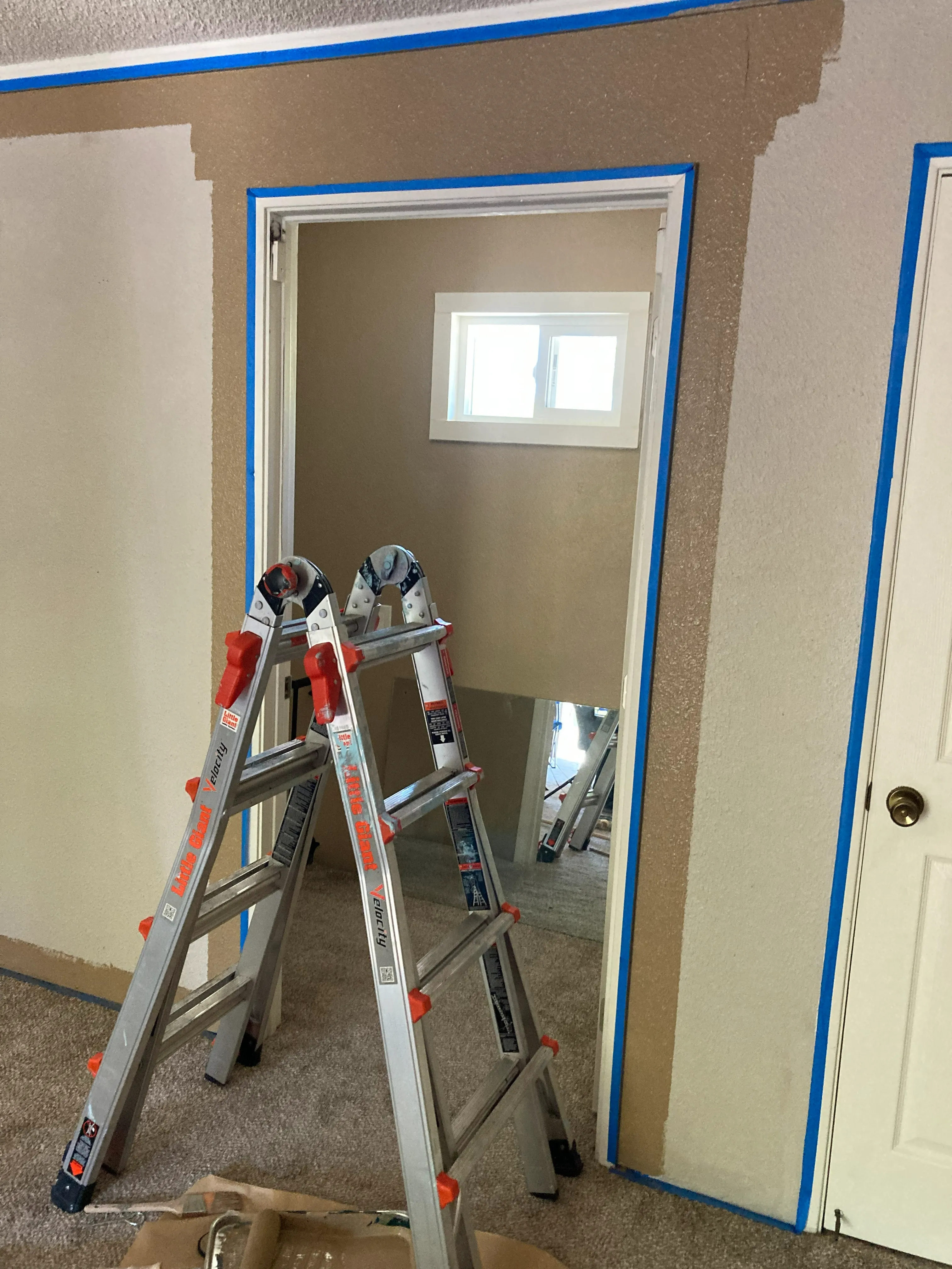 Aluminum step ladder in room with tape outlining a doorway being painted brown.
