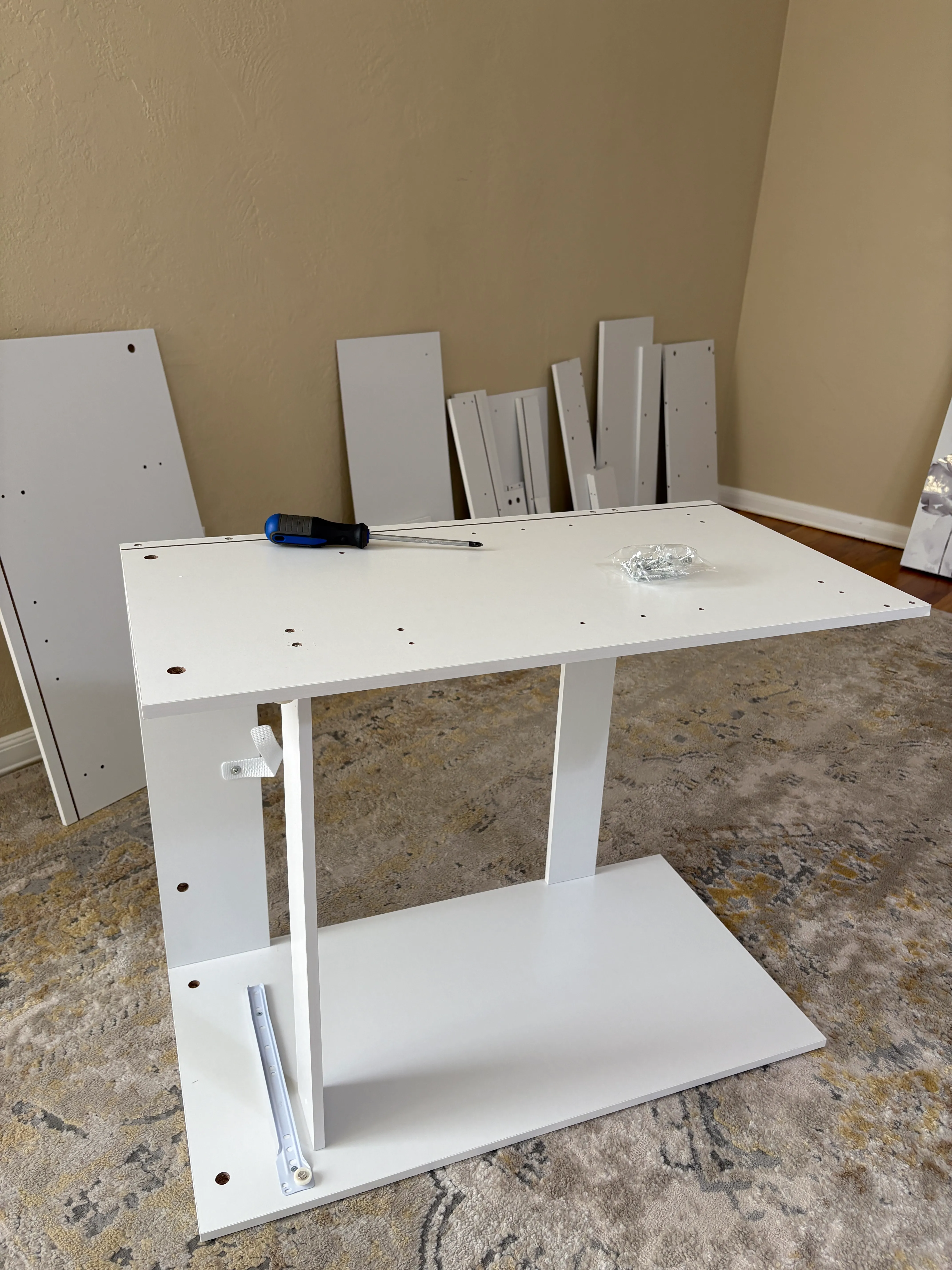 Partially assembled white furniture with a screwdriver and hardware on top on a carpeted floor.