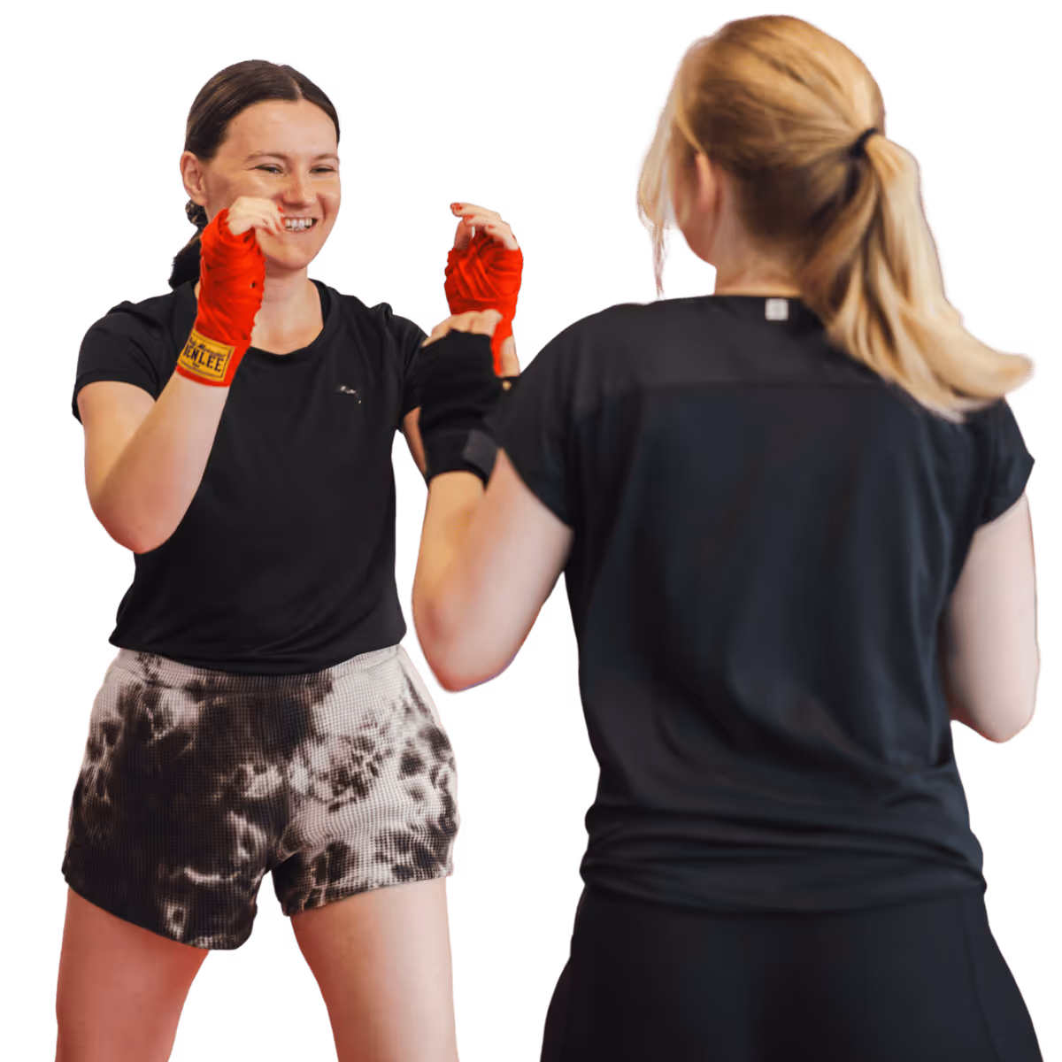 Zwei Frauen beim Boxtraining mit Handbandagen, eine lacht, die andere zeigt ihren Rücken.