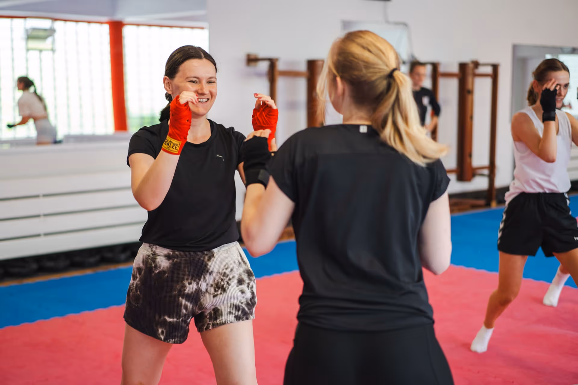 Zwei Frauen trainieren zusammen im Kampfsportstudio mit roten und schwarzen Handbandagen.