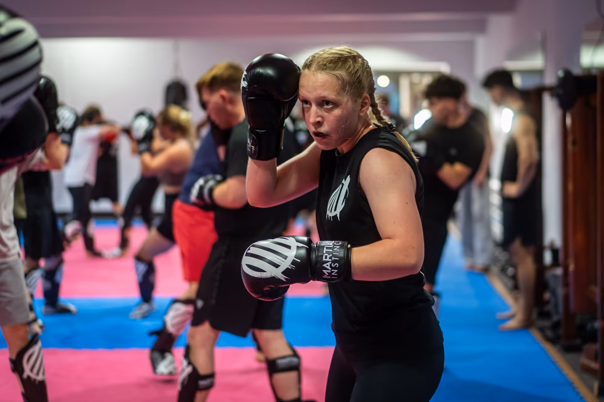 Frau mit Boxhandschuhen trainiert fokussiert im Kickboxkurs mit mehreren anderen Teilnehmern in einem Trainingsraum.