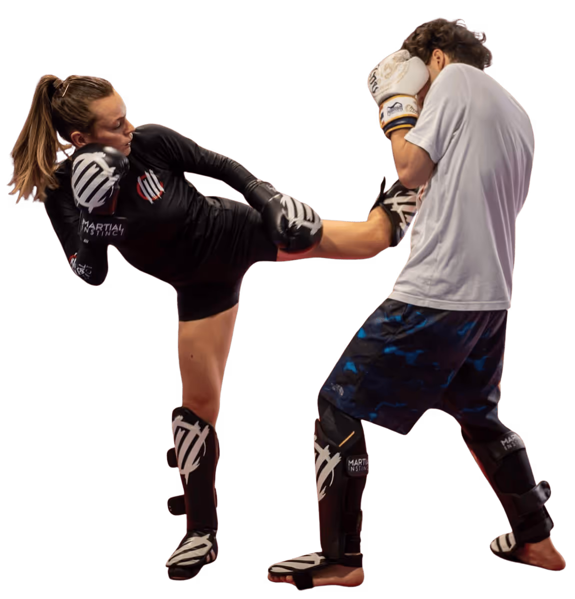 Frau führt einen hohen Kick gegen einen Mann im Kickboxen, beide tragen Schutzausrüstung und Boxhandschuhe.