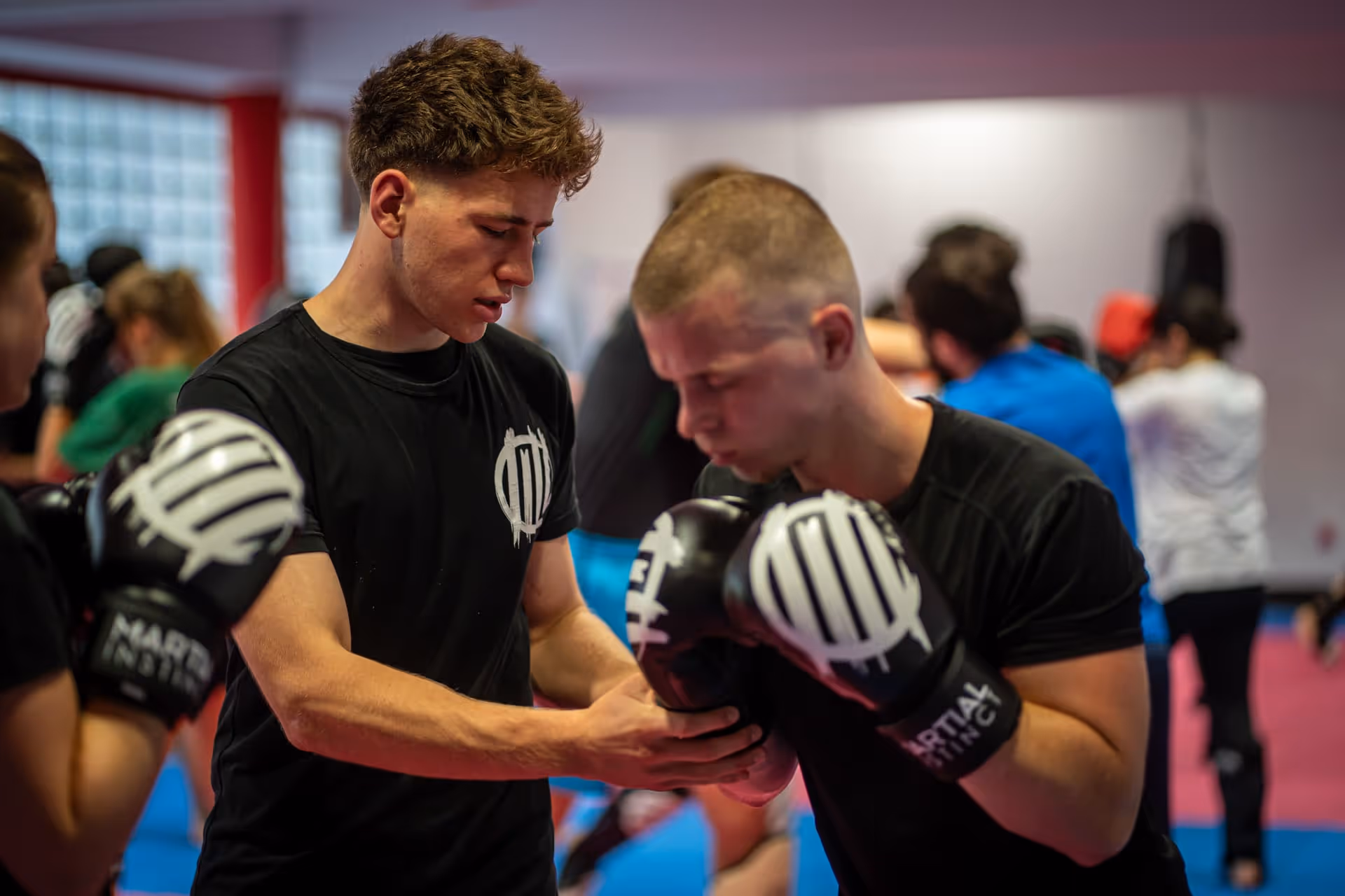 Zwei junge Männer in einem Kickboxtraining, einer korrigiert die Haltung des anderen mit Boxhandschuhen.