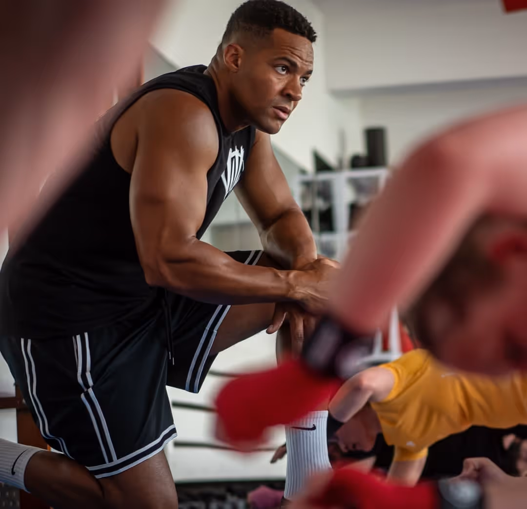 Mann in schwarzem Sportoutfit lehnt sich während eines Trainings im Fitnessstudio auf ein Knie.