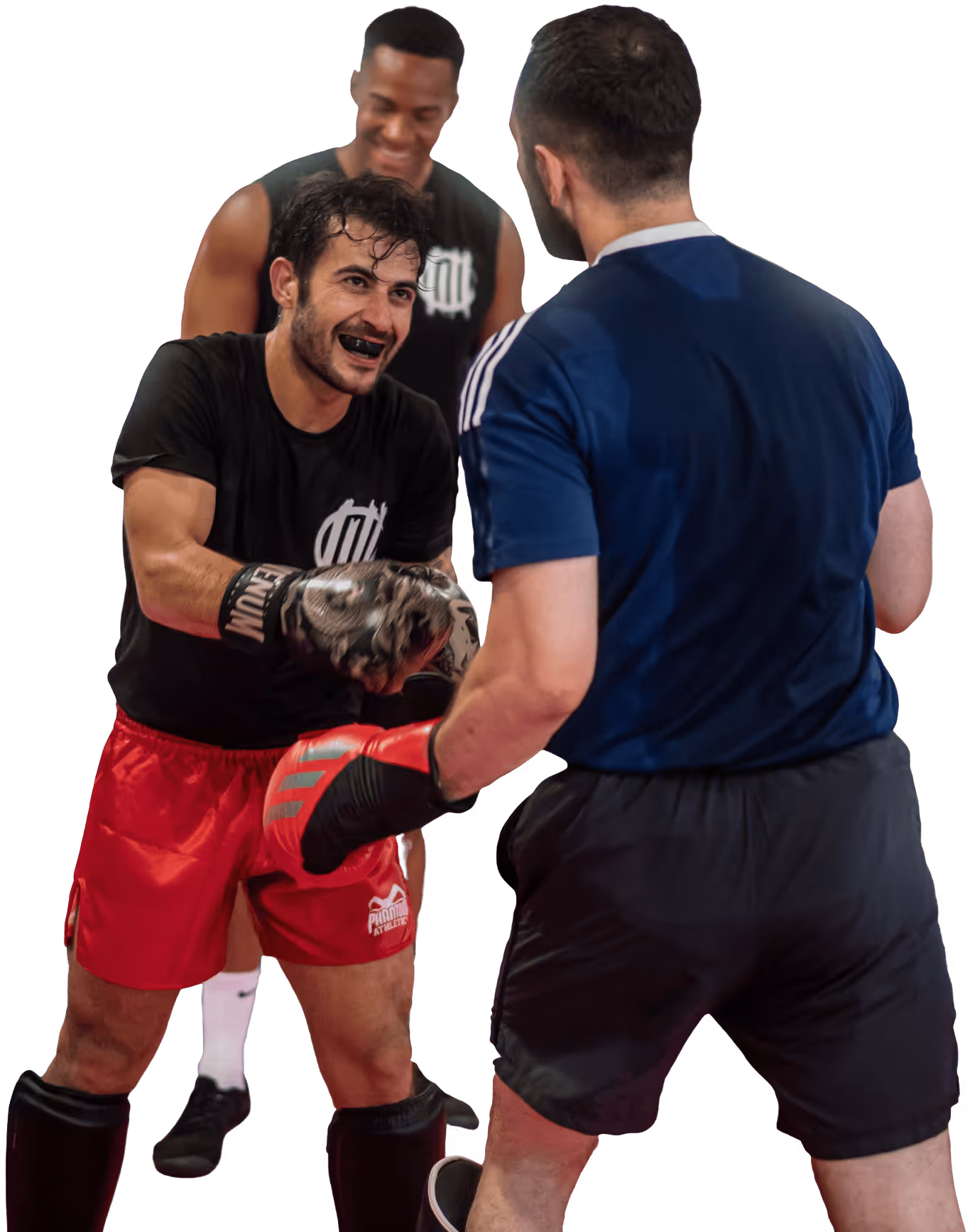 Zwei Männer mit Boxhandschuhen trainieren Kampfsport, während ein weiterer Mann im Hintergrund zuschaut und lächelt.