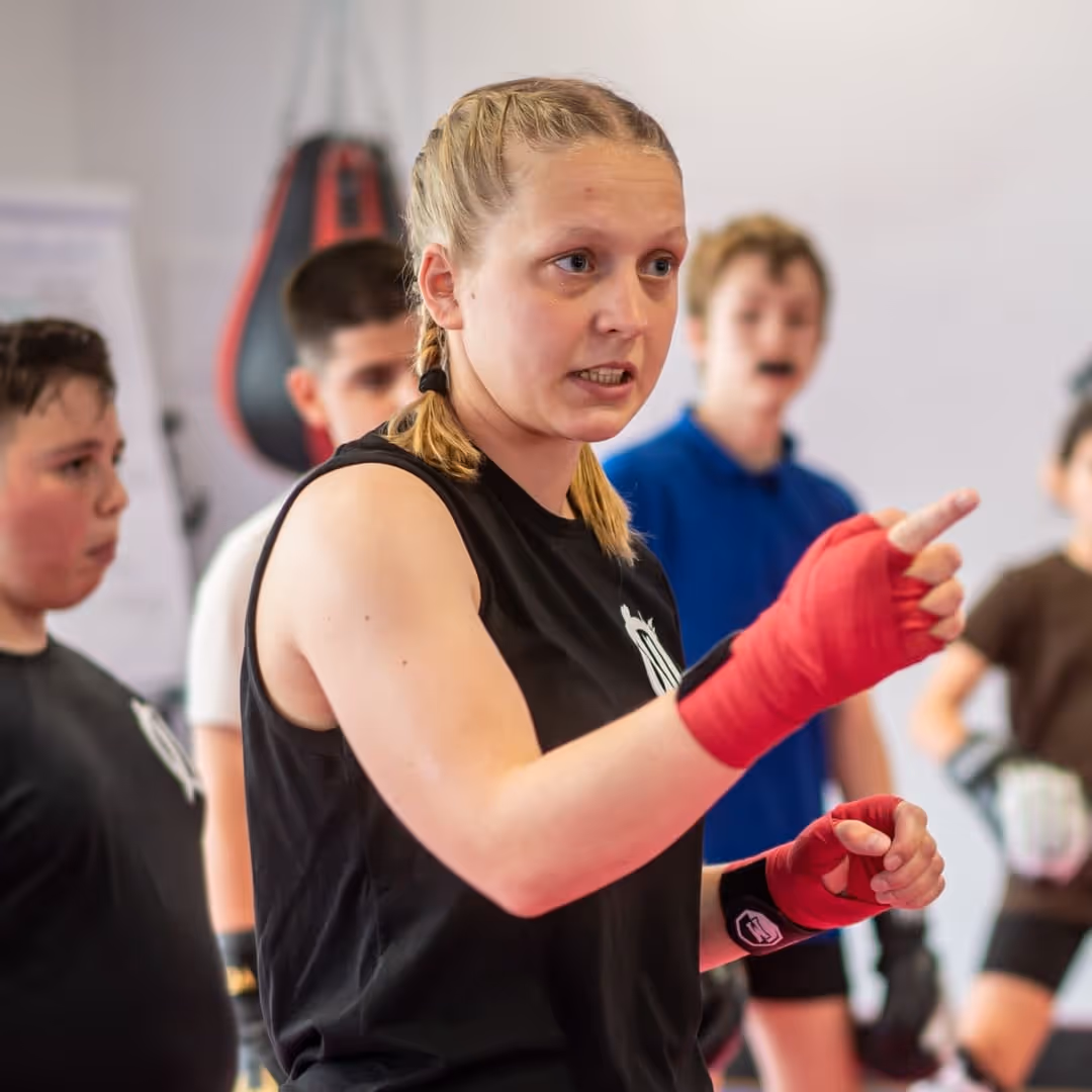 Frau mit roten Boxbandagen unterrichtet Jugendliche in einem Boxtraining.