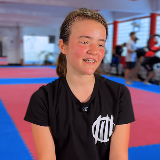 Lächendes Mädchen mit Zahnspange in schwarzem T-Shirt in einem Sportstudio mit roten und blauen Matten.