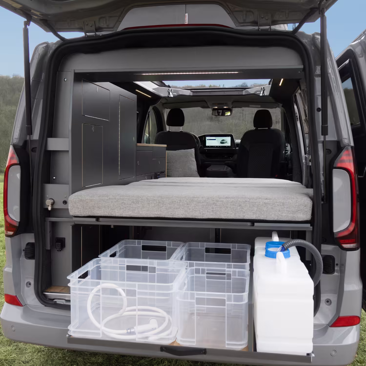 Innenansicht eines geöffneten Campers mit ausgezogenem Bett, schwarzen Schränken und transparenten Aufbewahrungsboxen im Heck.