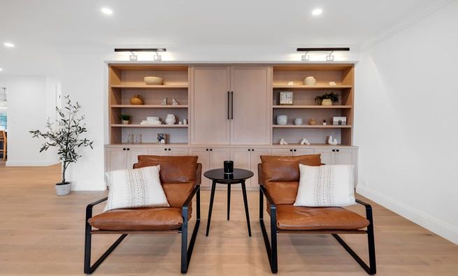 Modern living room with two brown leather chairs, a black round side table, and a built-in wooden shelving unit with decorative items.
