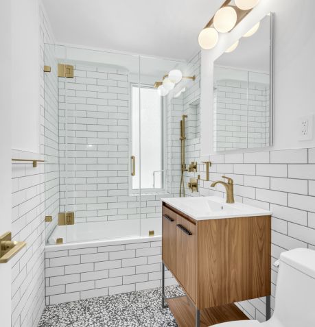 Modern bathroom with white subway tiles, a glass shower enclosure, wooden vanity with gold fixtures, and patterned floor tiles.