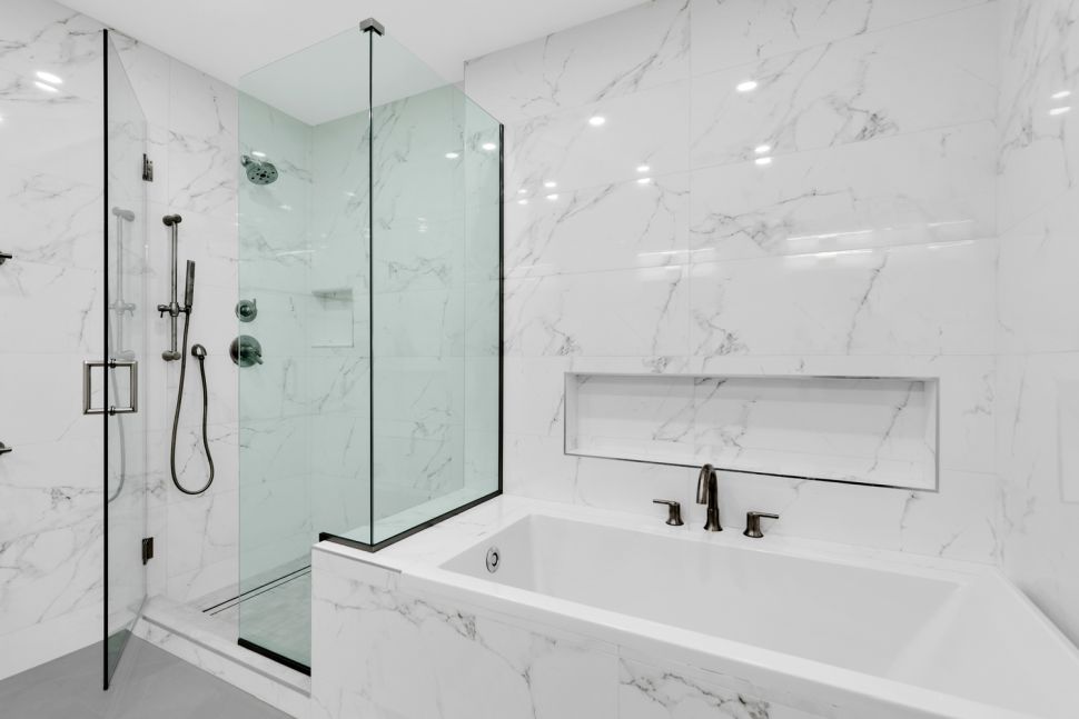 Modern bathroom with white marble walls, a glass-enclosed shower, and a built-in bathtub with bronze fixtures.