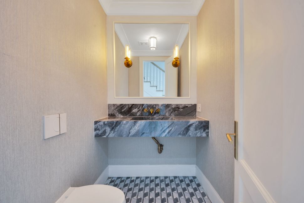 Small bathroom with a modern marble sink, large mirror, wall sconces, and geometric tiled floor.