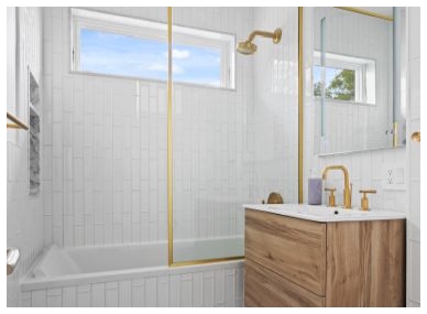 Modern bathroom with white tiled walls, a bathtub with glass shower door, gold fixtures, and a wooden vanity with a white sink.