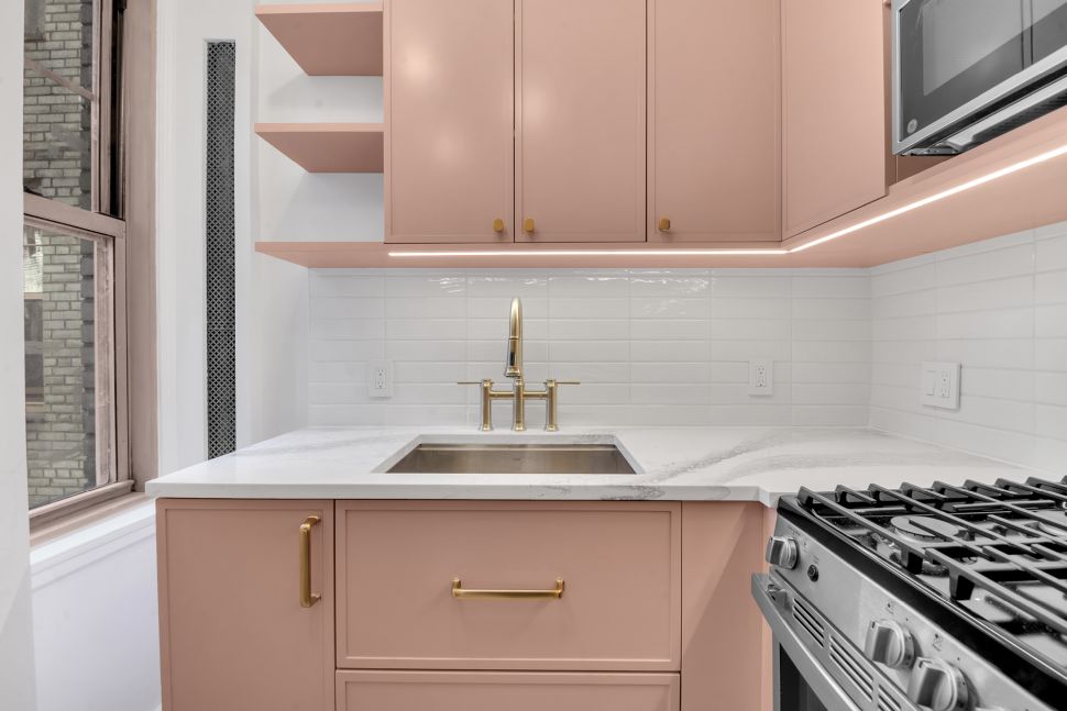 Modern kitchen with blush pink cabinets, white marble countertop, brass faucet, white subway tile backsplash, and stainless steel stove.