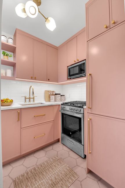 Modern pink kitchen with gold hardware, stainless steel stove, microwave, white countertop, and hexagonal floor tiles.