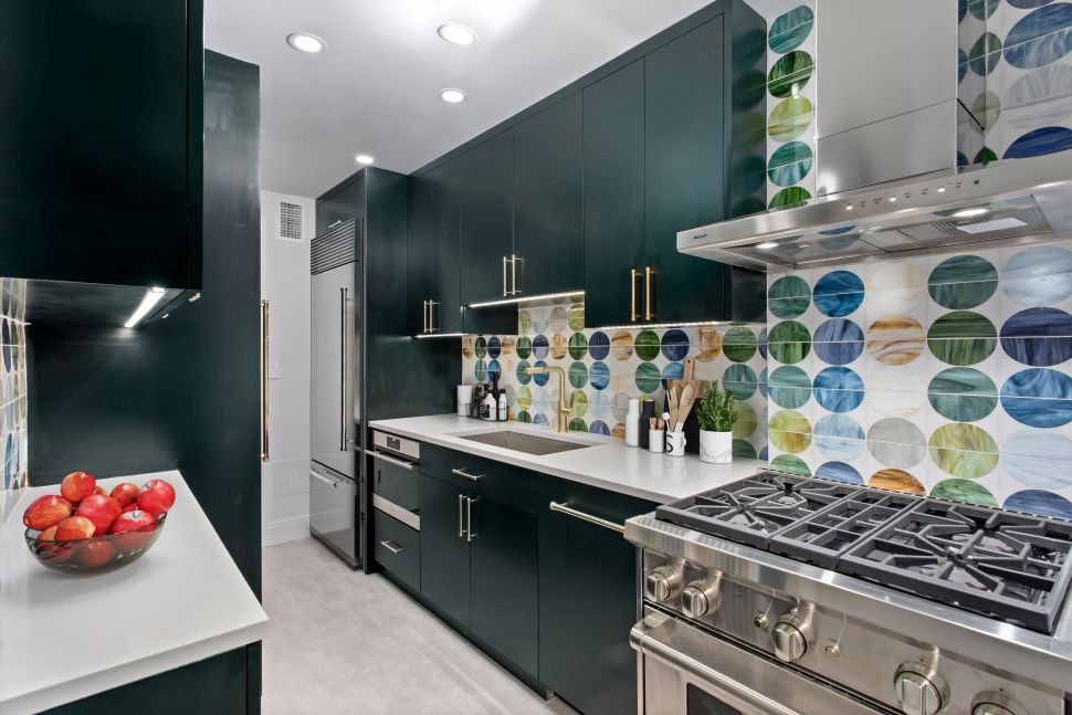 Modern kitchen with dark green cabinets, white countertops, stainless steel appliances, and a colorful circular-patterned tile backsplash.