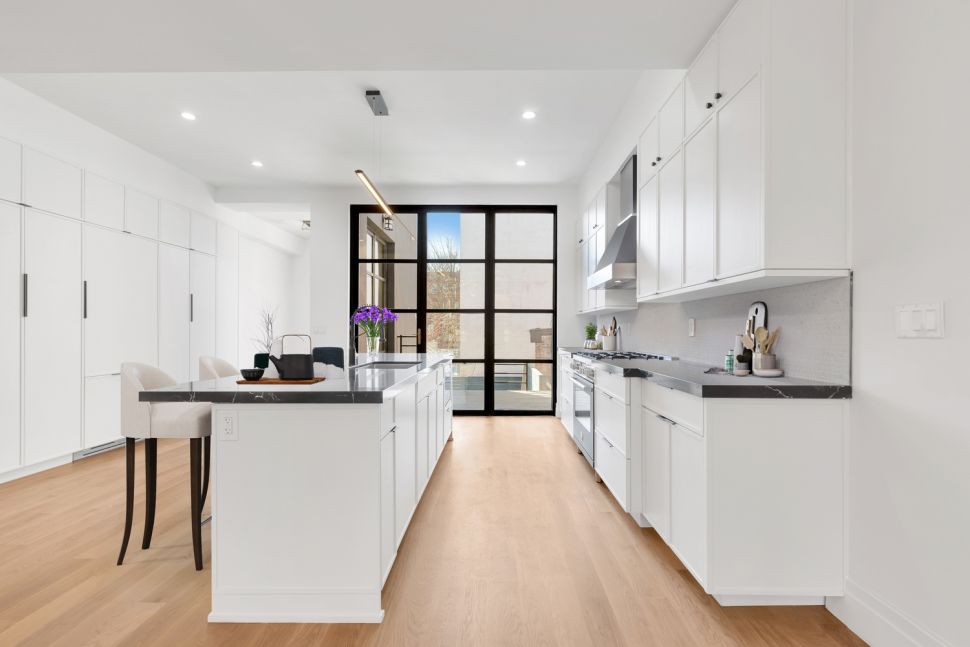 Bright modern kitchen with white cabinets, black countertops, light wood flooring, and a large window door letting in natural light.