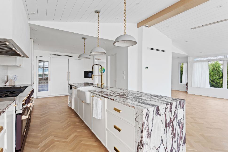Bright modern kitchen with a large marble island, gold fixtures, and wood parquet flooring.