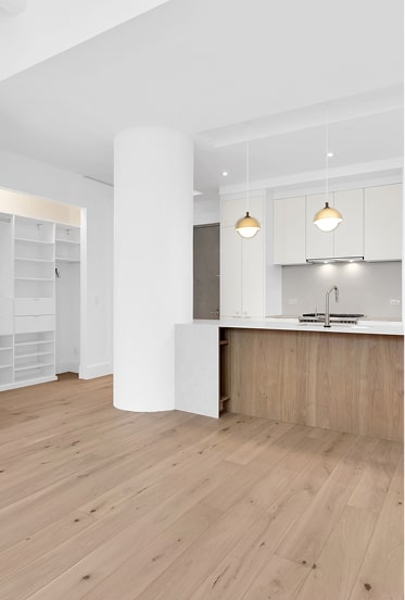 Modern kitchen with wooden floor, white cabinets, a large round pillar, and an island with a wooden front and two pendant lights.