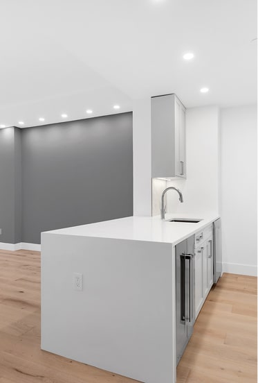 Modern minimalist kitchen with white countertops, light wood flooring, and a gray accent wall.