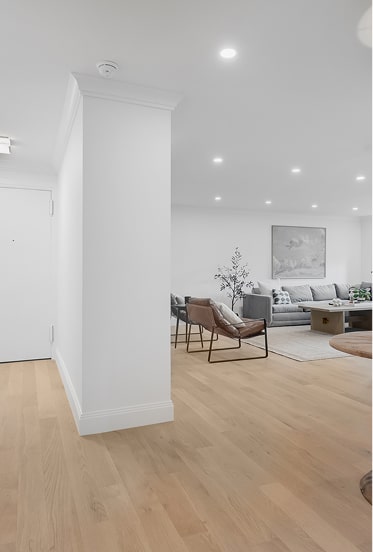 Modern living room with light wood flooring, white walls, a gray sofa, two brown leather chairs, a coffee table, and a large painting on the wall.