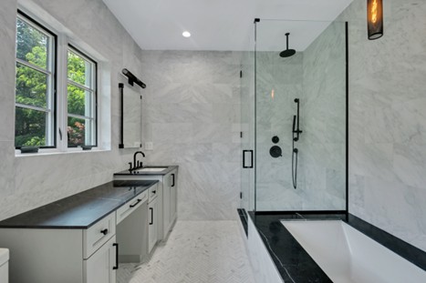 Modern bathroom with double sink vanity, large windows, and a glass-enclosed shower over a bathtub.