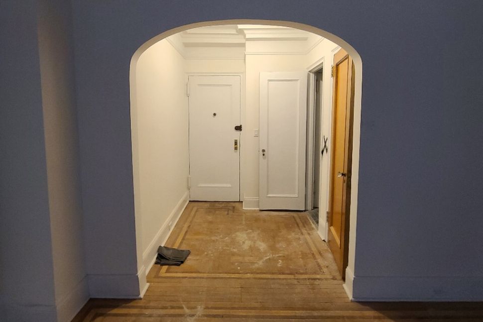 Empty hallway with an arched doorway, white walls, closed white door at the end, and a wooden door on the right side.