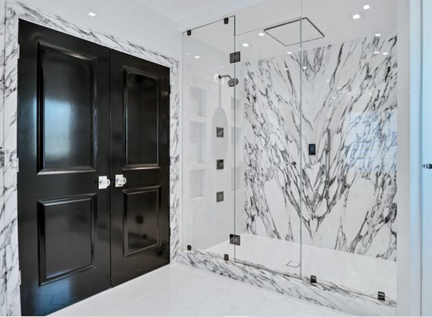 Modern bathroom with large glass-enclosed shower featuring white marble walls with gray veining and black double doors.