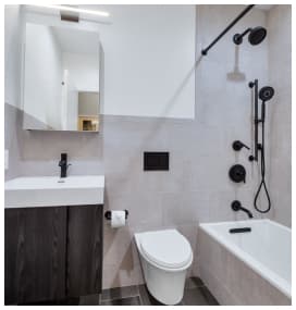 Modern bathroom with white walls, a dark wood vanity with a white sink, wall-mounted toilet, and bathtub with black fixtures.