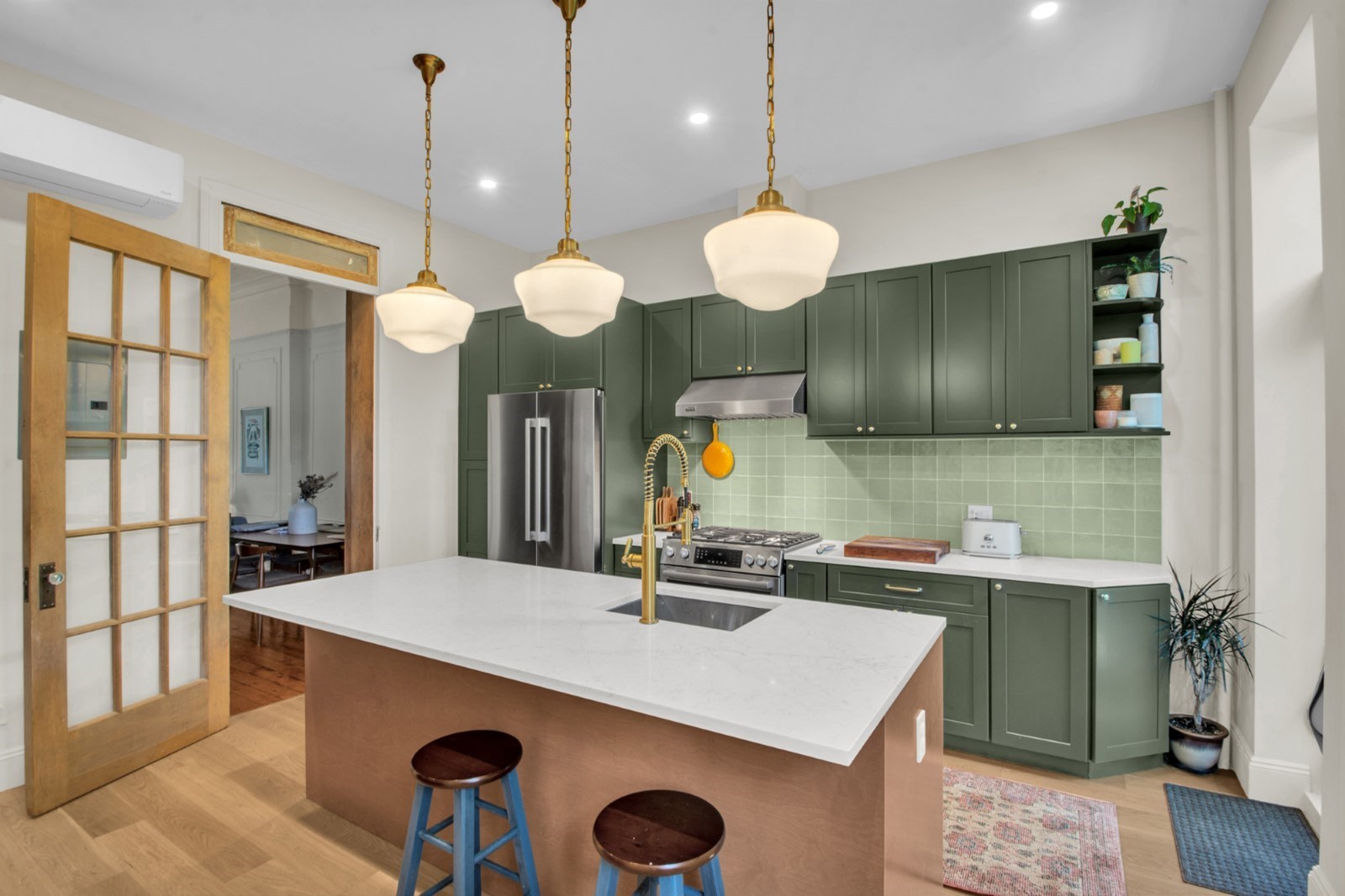 Modern kitchen with green cabinets, white island countertop with gold faucet, stainless steel appliances, and three pendant lights.