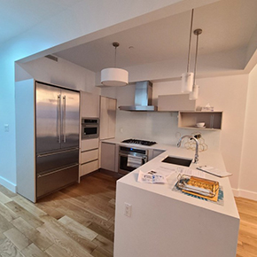 Modern kitchen with stainless steel refrigerator, built-in oven, gas stove, white countertops, and wooden floor.