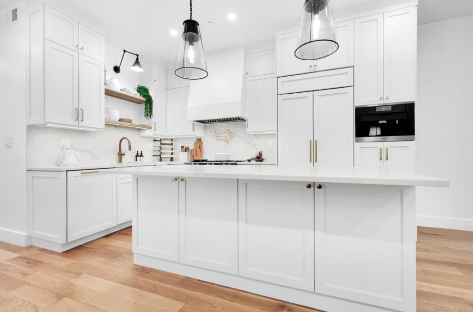 Bright modern kitchen with white cabinets, a large island, wood flooring, and pendant lighting.