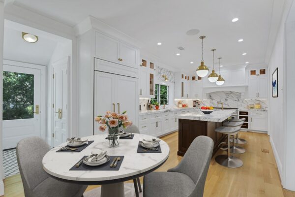 Modern kitchen with white cabinetry, marble countertops, an island with bar stools, and a round dining table set with flowers and place settings.