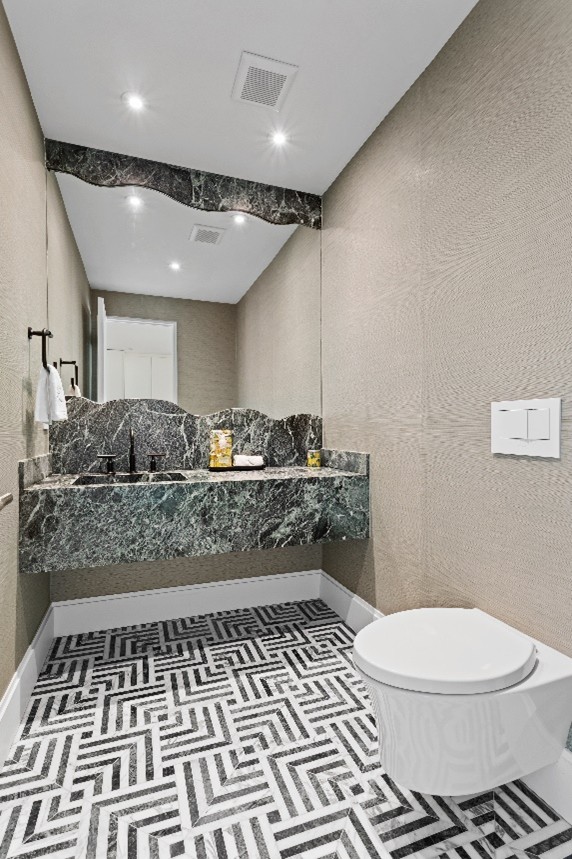 Modern bathroom with a wall-mounted marble sink, large irregular-edged mirror, black faucet, patterned black and white floor tiles, and a white wall-mounted toilet.