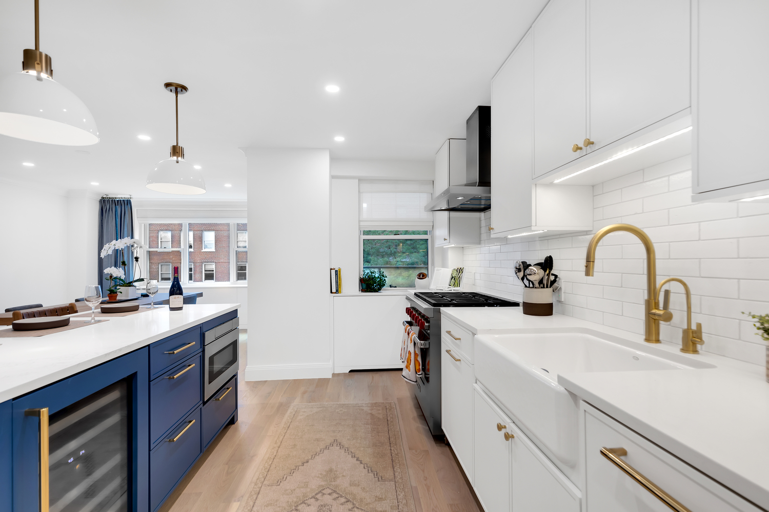 Modern kitchen with white cabinetry, gold fixtures, a blue island with built-in wine cooler, and hardwood floors.