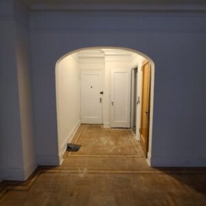 Empty hallway with arched entrance, parquet floor, and closed white doors at the end.