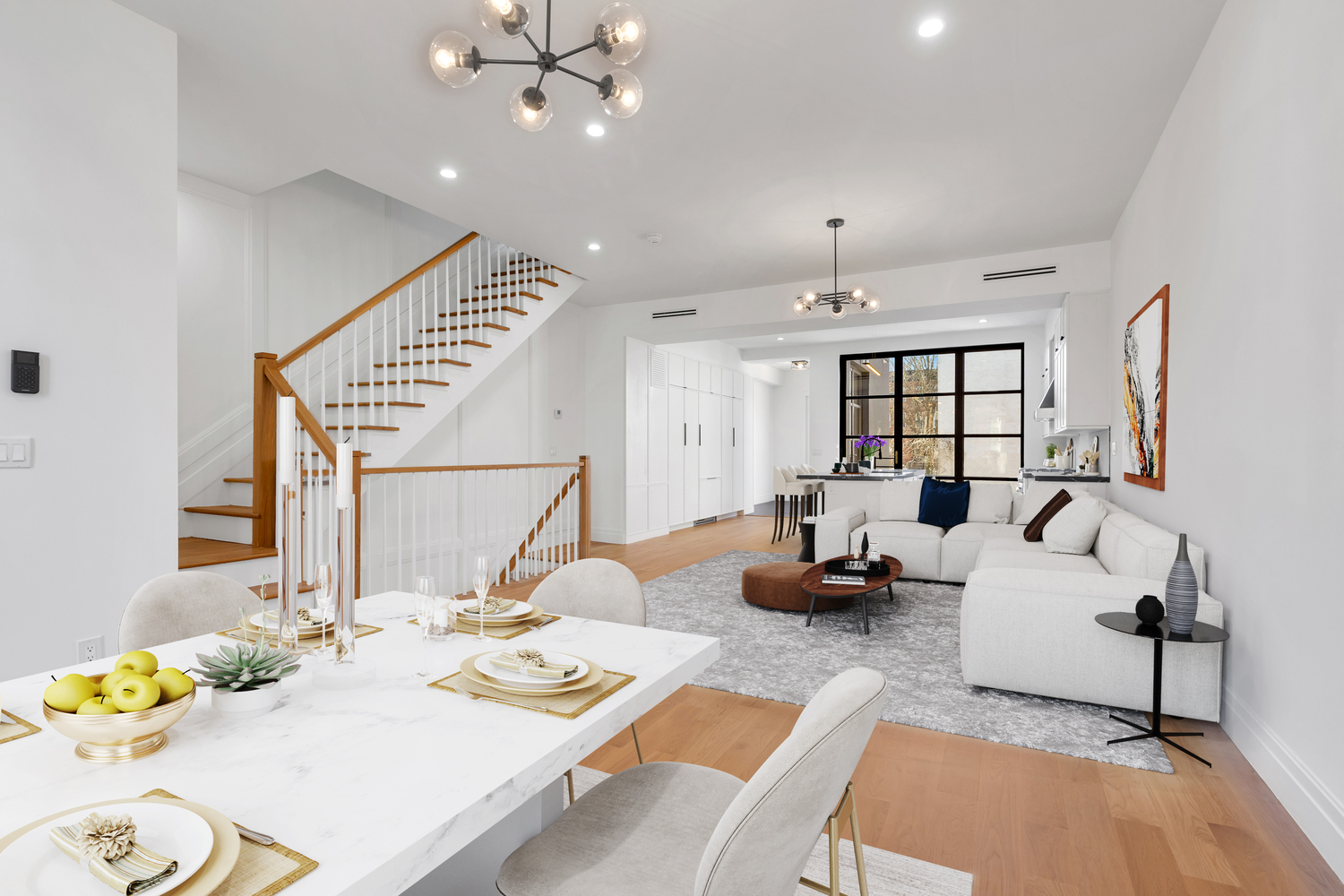 Bright modern open-concept living and dining area with white walls, wood floors, a dining table set for four, a white sectional sofa, and a staircase with wooden handrails.