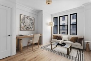 Modern living room with white sofa, decorative pillows, wooden desk with chair, floor lamp, and abstract wall art.