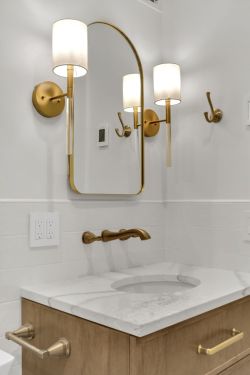 Modern bathroom vanity with a marble countertop, gold faucet, gold-framed mirror, and two wall-mounted lights with white shades.