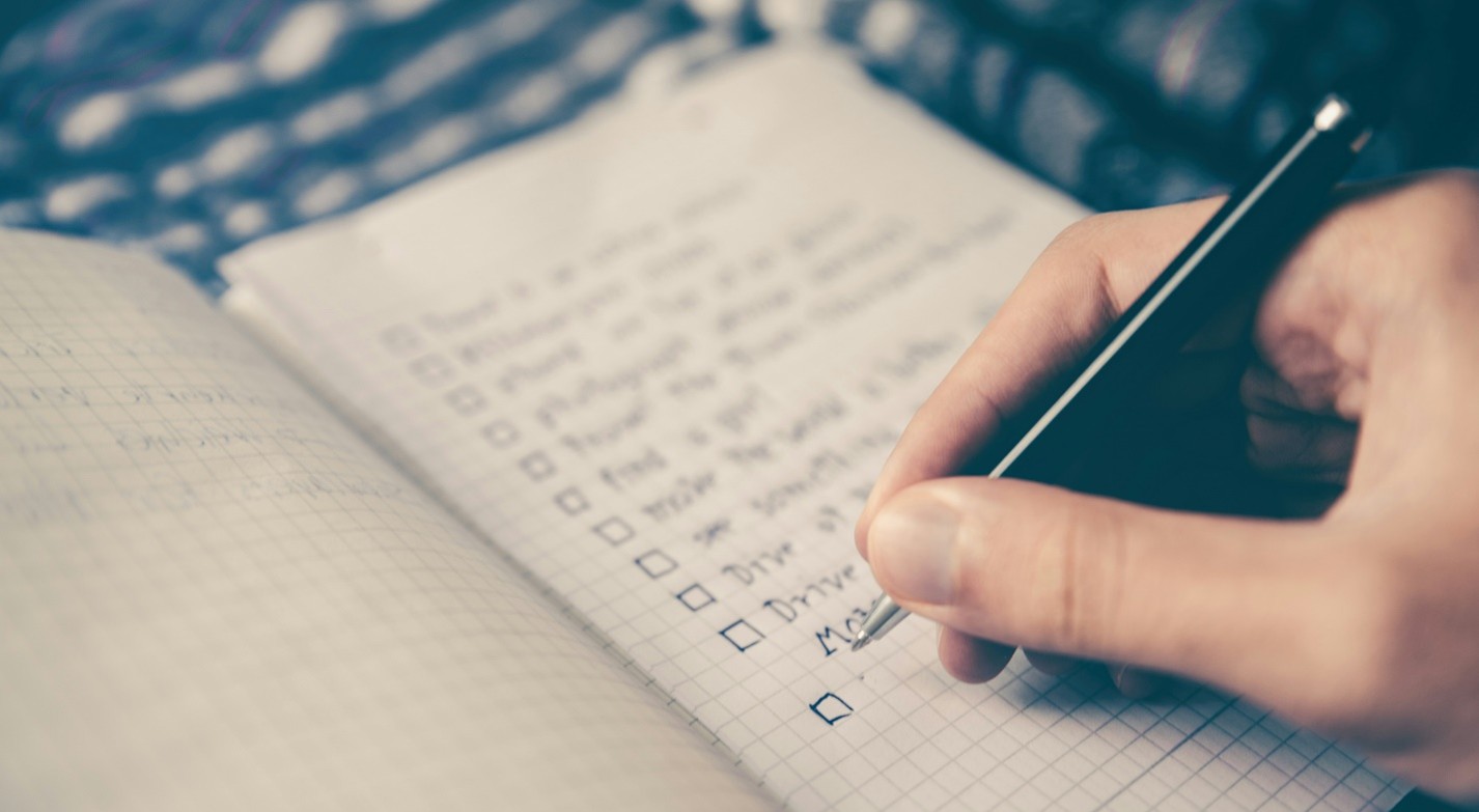Close-up of a hand writing a checklist in a notebook with squared paper.